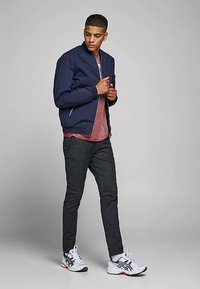 Navy bomber jacket over a light pink t-shirt, paired with dark textured pants and white sneakers with black accents.