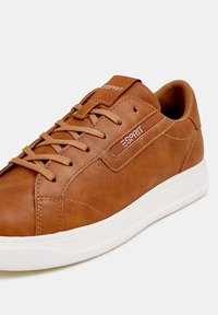 Brązowy skórzany sneaker z białą gumową podeszwą, okrągłym noskiem, płaskimi sznurowadłami i logo na boku. Wyróżnia się przeszyciami i perforacjami na cholewce.