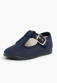 Zapato de tela azul marino con superficie texturizada, correa con hebilla y detalle recortado. Presenta una suela plana negra y un forro interior beige.