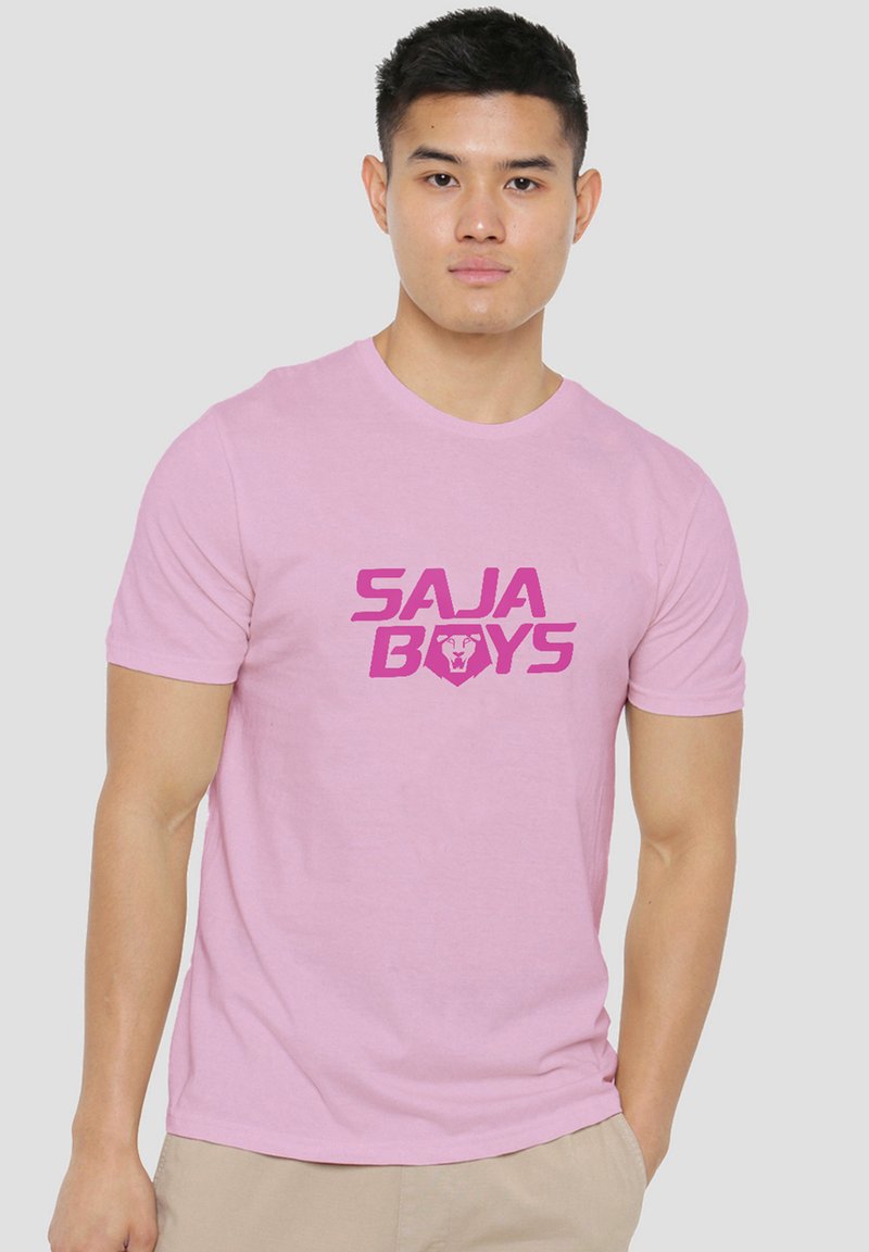 Young man wearing a light pink t-shirt with "SAJA BOYS" and a lion logo printed in bold pink on the front.