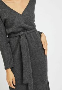 Šedé obálkové šaty z jemné, strukturované tkaniny s hlubokým výstřihem do V, dlouhými rukávy a páskem na zavázání v pase. Obsahují boční kapsy.
