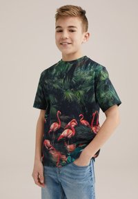 Kortärmad skjorta med en mörkgrön bakgrund och ett livligt mönster av rosa flamingos, omgiven av grönska. Tillverkad av bomull.