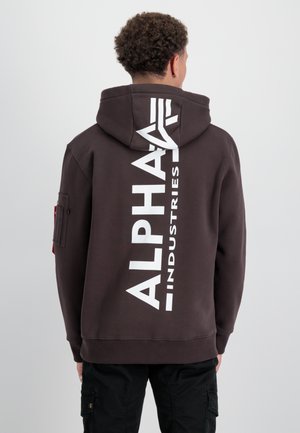 Barna kapucnis pulóver, nagy fehér logóval a hátán, amelyen az "ALPHA INDUSTRIES" felirat szerepel, húzózsinórral ellátott kapucnival és oldalsó zsebbel.