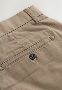 Pantalon en tissu beige avec une poche arrière à fermeture par bouton et une passants de ceinture à la taille.