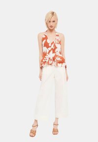 Top halter floreale arancione e bianco, con un design fluido. Abbinato a pantaloni bianchi a gamba larga e sandali con tacco marroni.