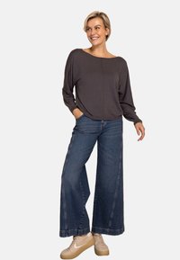 Dunkelgraues Langarmshirt kombiniert mit weitem Denim-Jeans. Hellbeige Sneaker mit dezenten Akzenten. Glatter Stoff und saubere Nähte.