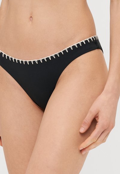Juodas bikini dugnas su kreminiu zigzagu siuvinėjimu aplink juosmenį. Turi žemą liemenį ir sklandžią tekstūrą.