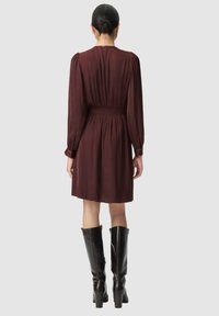 Robe mauve à manches longues, taille smockée et détails plissés, associée à des bottes noires à talons jusqu'aux genoux. Tissu lisse et fluide.