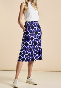 Sinivalkokuvioinen hame, jossa joustava vyötärö, kerroksellinen muotoilu ja sivutaskut, yhdistettynä valkoiseen hihattomaan toppiin ja valkoisiin tennareihin.