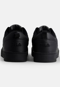 Baskets noires en cuir, avec une texture lisse, un col rembourré et un logo emblématique sur le talon. Design basse avec semelles plates.