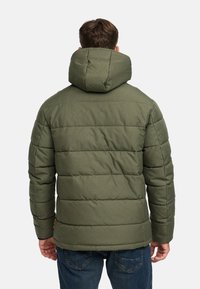 Giacca a vento verde con cappuccio, caratterizzata da motivi trapuntati, tessuto testurizzato e vestibilità slim. Mostrata da dietro, abbinata a jeans blu.