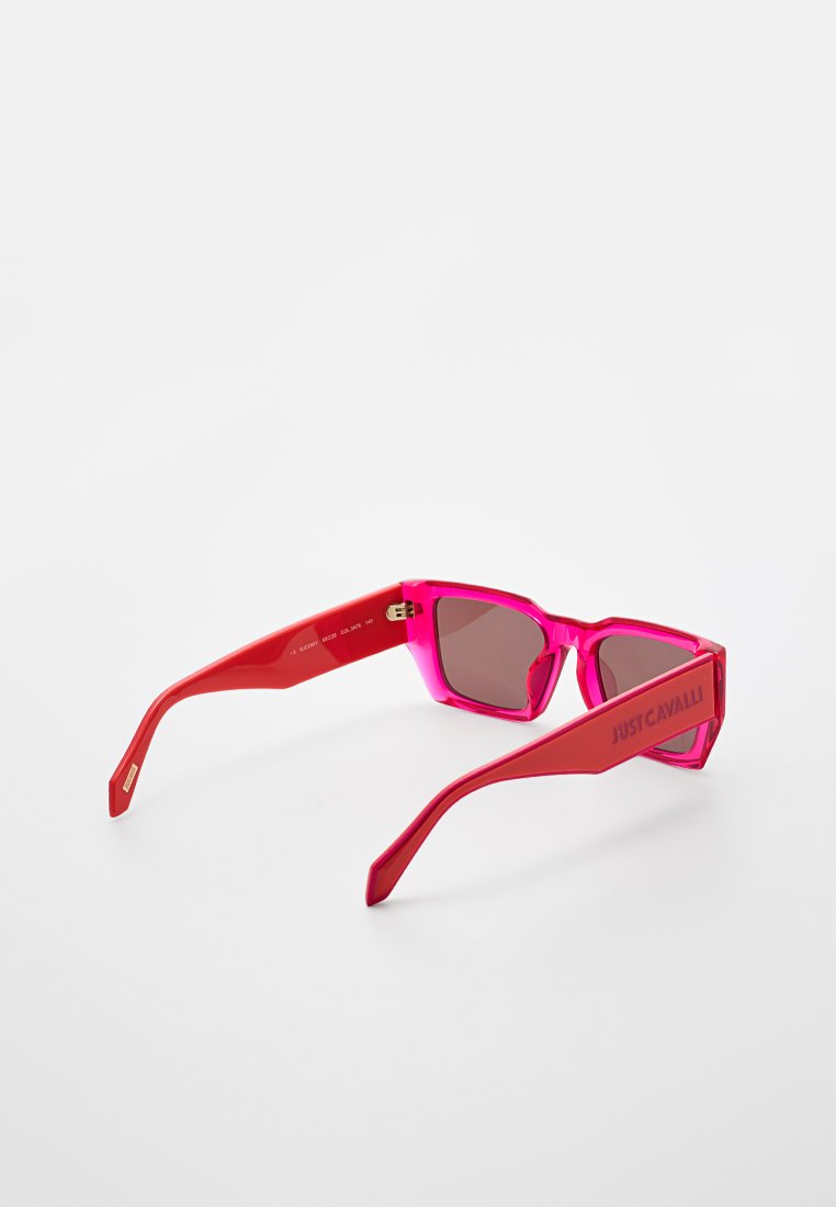 Des lunettes de soleil rectangulaires rouges et roses avec des verres marron, présentant des montures en plastique épaisses et le logo "JUST CAVALLI" sur le côté.