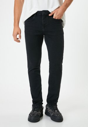 Jeans negros ajustados de mezclilla, con un diseño clásico de cinco bolsillos, cierre de botón y una sutil textura desgastada.