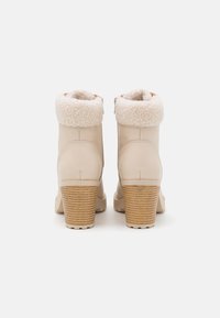 Beige kotníkové boty s límcem podšitým ovčí vlnou, texturovaným zvýšeným podpatkem, hladkým koženým povrchem a elegantním zaobleným špičkovým designem.