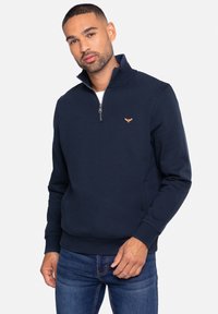 Navy zip-up sweatshirt gemaakt van zachte stof, met een staande kraag, geribbelde manchetten en een klein gouden logo op de borst.