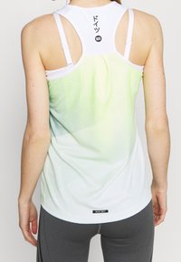 Achteraanzicht van een dames tanktop in wit en lichtgroen verloop, met dunne bandjes, gestructureerde stof en een zwart "HEAT.RDY" label aan de zoom.