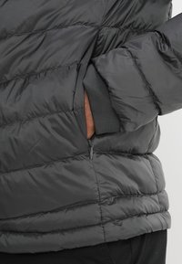 Mustapuffatakki, jossa on poimutettu pinta, sivussa vetoketjullinen tasku ja elastiset hihansuut tiivistä istuvuutta varten.