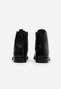 Botas de cuero negro hasta el tobillo con una textura suave, punta redondeada y un tacón bajo. Presentan una cremallera lateral y una lengüeta en la parte trasera.