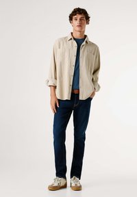 Bežová kordová košeľa, modré tričko, tmavé džínsy, svetlé topánky s akcentmi. Funkcie otvorený golier a vyhrnuté rukávy.