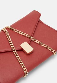 Borsa a pochette rossa con texture, dotata di una tracolla dorata e una chiusura rettangolare. Presenta un design pieghevole diagonale.