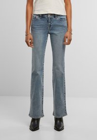 Blauwe flared jeans van middelmatig denim met een vervaagde afwerking; voorzien van vijf zakken en stikseldetails; gedragen met zwarte gehakte laarzen.