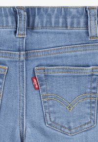 Világoskék farmernadrág arany varrással, két hátsó zsebbel és piros címkével. Jellemzően ívelt zsebkialakítással rendelkezik.