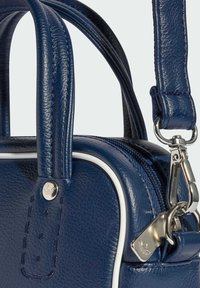 Tamno plava torba od teksturirane kože s dvostrukim ručkama, odvojivim remenom, srebrnim hardverom i kontrastnim bijelim obrubom. Ima zatvaranje na patentni zatvarač.