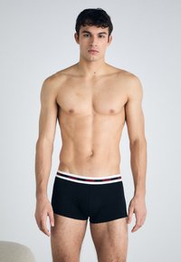 Boxeri negri, din material elastic, cu un brâu alb și roșu, inscripționat cu "HUGO". Materialul pare neted și se mulează pe corp, oferind o siluetă modernă.