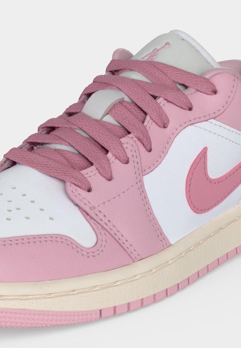 Rosa-weißer Sneaker mit niedrigem Schaft, rosa Schnürsenkeln, rosa Nike-Swoosh und perforierter Zehenkappe auf heller Sohle.