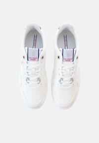 Zapatillas deportivas blancas con detalles perforados, cordones planos y lengüeta con marca. Suela de goma y diseño minimalista.
