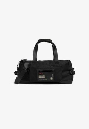 Borsa duffel rettangolare nera con due manici, cintura regolabile per la spalla, tasca anteriore con cerniera e un'etichetta con testo rosso e codice a barre.