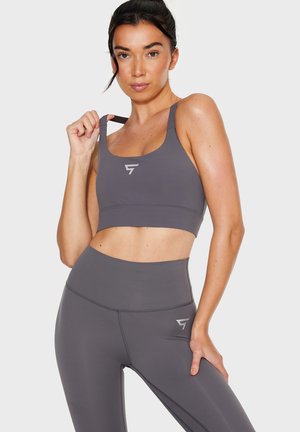 Gray sports bra and high-waisted leggings made from stretchy fabric, featuring a minimalistic design and logo accents. Smooth texture.