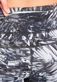 High-waisted leggings in a geometric pattern of black, gray, and white; features a zippered pocket and textured fabric with flat seams.