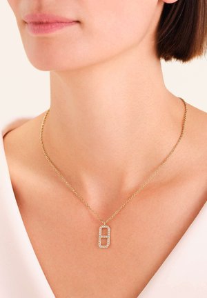 Zlatna ogrlica s lancem i pravokutnim privjeskom ukrašenim prozirnim cirkonima, s poliranim metalnim završetkom i geometrijskim dizajnom.