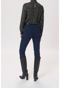 Granatowe dopasowane dżinsy z tylnymi kieszeniami, w zestawieniu z czarną wzorzystą bluzką z wysokim kołnierzem i wycięciem oraz czarnymi kozakami za kolano.