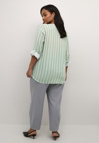 Mint green shirt with vertical gray stripes, rolled cuffs, paired with light gray pants and black heeled sandals. Smooth fabric texture.