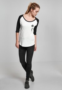 White and black raglan t-shirt featuring a floral graphic, paired with black skinny jeans and black textured sneakers; casual outfit.