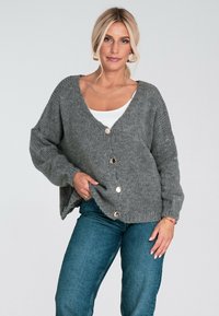 Szary sweter robiony na drutach z dekoltem w kształcie litery V, długimi rękawami i złotymi guzikami z przodu. Posiada luźny krój i miękką teksturę.