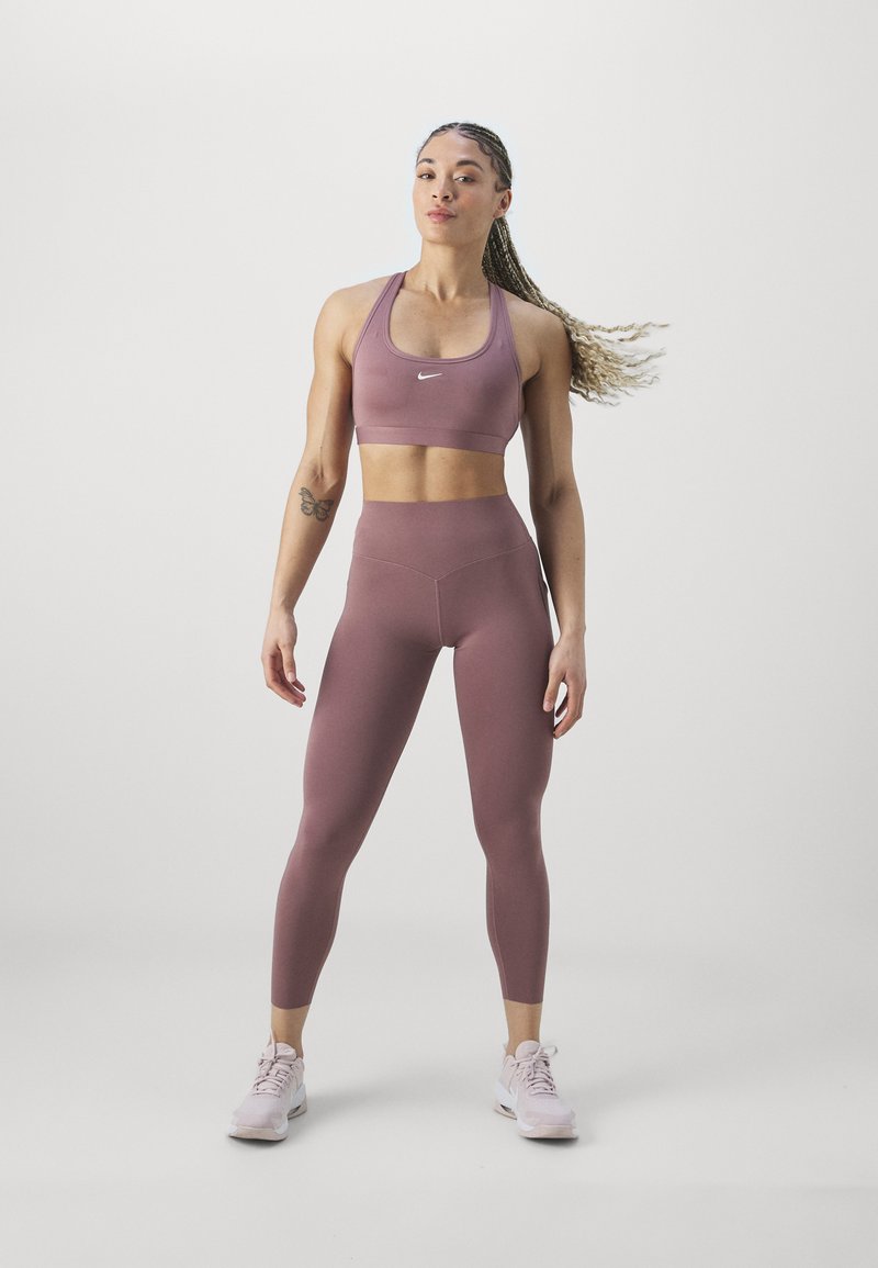 Reggiseno sportivo e leggings a vita alta in morbido tessuto rosa. Il reggiseno presenta spalline larghe e il logo Nike; i leggings sono lisci, aderenti con dettagli di cucitura.