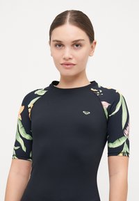Čierny rash guard s krátkymi rukávmi so vzorom kvetín v zelenej, oranžovej a ružovej farbe. Obsahuje malé logo v oblasti hrudníka.