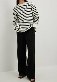 Camicia a maniche lunghe a righe bianche e nere con una vestibilità rilassata, abbinata a pantaloni neri a vita alta con gamba ampia e sandali neri a scivolo.