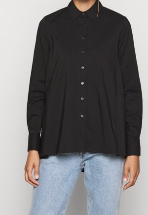 Zwarte blouse met lange mouwen en knopen, los gedragen over lichtblauwe spijkerbroek, met kraag en manchetten zichtbaar, zonder zichtbare patronen of logo's.