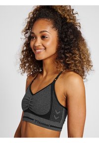 Grå sportbh med en sammanpressad framdel, nätaccenter, justerbara band och logodetaljer vid midjan. Mjuk, texturerad tyg.