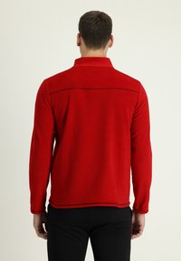 Pullover in pile rosso con colletto, dotato di maniche lunghe e cuciture a contrasto lungo la cucitura della spalla. Texture liscia, vestibilità rilassata.