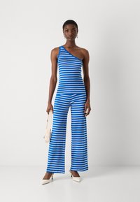 Randig blå jumpsuit med en axel, som har en figursydd topp och vida byxor; slät yta och kontrasterande vita ränder.