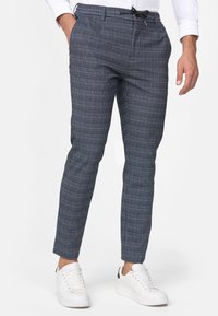 Niebieskie, zwężane spodnie w kratę z talią ze ściągaczem, wykonane z tkaniny tkanej. Połączone z białymi trampkami dla casualowego wyglądu.