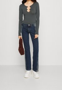 Langärmeliger, dunkelgrauer Body mit drei ovalen Ausschnitten am Ausschnitt. Dunkelblaue, gerade Jeans und klobige weiße Plateaustiefel. Braune, flauschige Tasche.