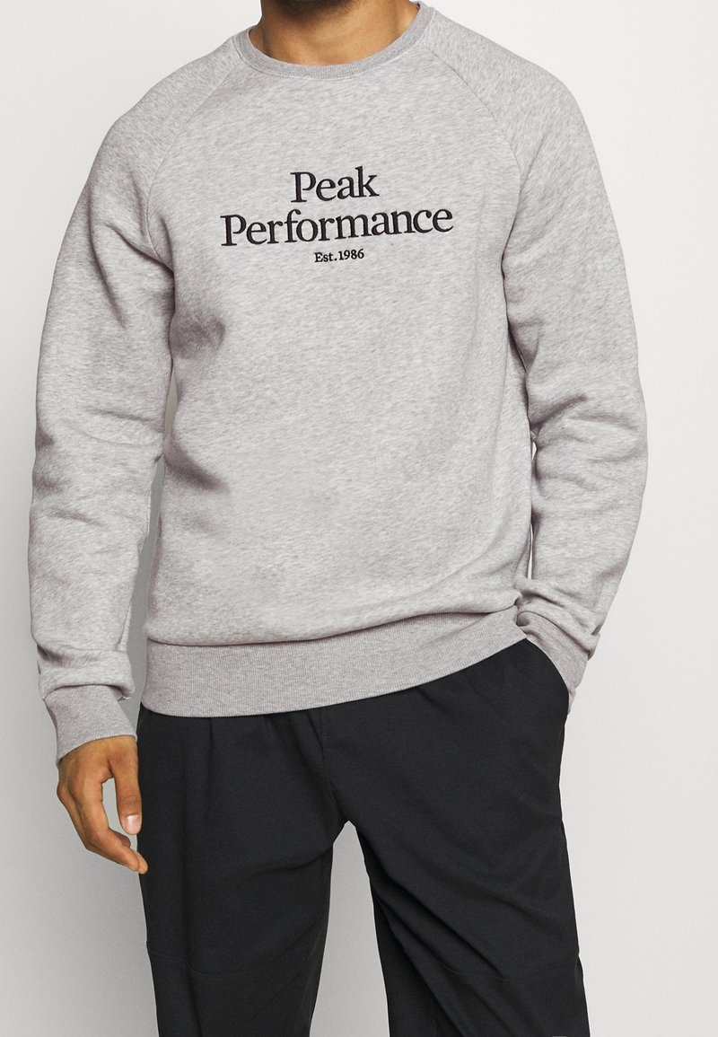 Felpa grigia in cotone con maniche raglan e collo rotondo. Al centro, il testo nero recita "Peak Performance" con "Est. 1986" sottostante.