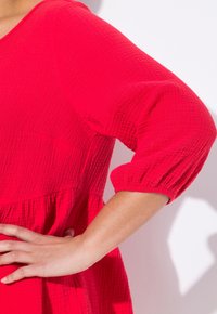 Vestito rosso testurizzato con maniche a tre quarti e design svasato. Il tessuto sembra leggero con un sottile motivo a costine.