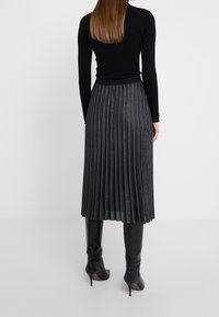 Top de manga larga negra combinado con una falda plisada de largo a larodilla en tejido gris oscuro con rayas metálicas y una textura lisa.